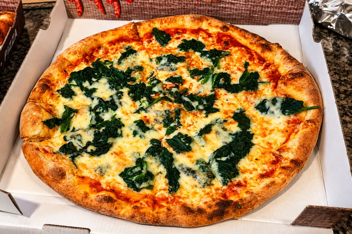 Pizza mit Spinat und geschmolzenem Käse im Karton