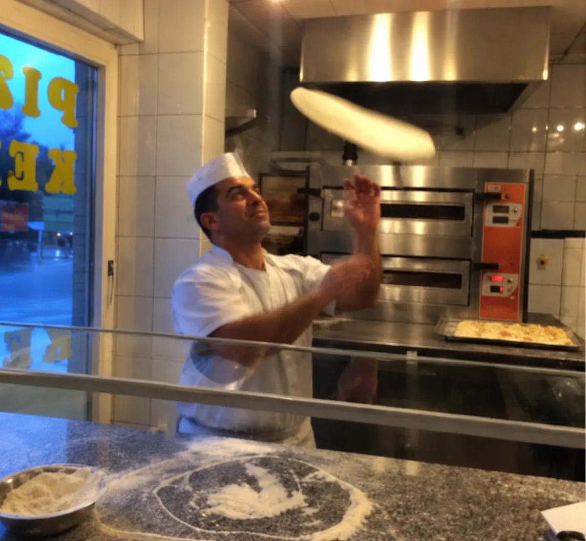 Der Pizzabäcker wirft in der Dostlar-Küche den Pizzateig in die Luft